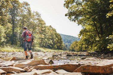 Sırt çantası konsept görüntüsüyle seyahat. Dağ nehrinden geçen yürüyüş botu giyen bir gezgin. Yaz gezisi sırasında dağlarda yürüyüş yapan bir adam. Tatil gezisi doğaya yakın. Doğal manzara.