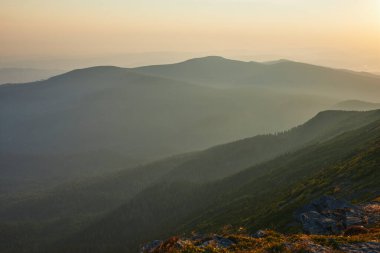 Dağlarda gün doğumu. Aydınlatılmış sisli tepeleri, sisli yamaçları ve vadileri olan doğal dağ manzarası, turuncu sarı güneş ışığıyla mavi gökyüzü. Polonya 'dan Beskid Zywiecki' den inanılmaz bir sahne
