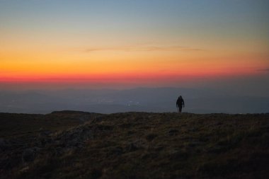 Adam güneşin doğuşuna bakıyor. Gün doğumunda dağlar. Zirvede duran adam. Aydınlatılmış sisli tepeleri, sisli yamaçları ve vadileri olan doğal dağ manzarası, turuncu sarı güneş ışığıyla mavi gökyüzü. Polonya 'dan Beskid Zywiecki' den inanılmaz bir sahne