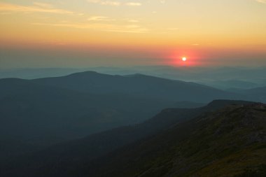 Dağlarda gün doğumu. Aydınlatılmış sisli tepeleri, sisli yamaçları ve vadileri olan doğal dağ manzarası, turuncu sarı güneş ışığıyla mavi gökyüzü. Polonya 'dan Beskid Zywiecki' den inanılmaz bir sahne