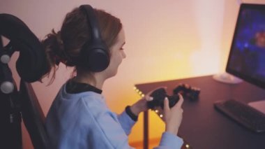 Evde video oyunu oynayan ergen kız. Oyuncular ekranın önünde oyun kağıtlarını tutuyorlar. Karanlık odada oynayan flamalar neon ışıklarıyla aydınlatılıyor. Rekabet ve eğlence.