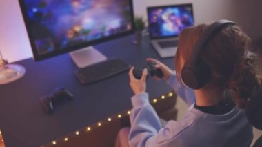 Evde video oyunu oynayan ergen kız. Oyuncular ekranın önünde oyun kağıtlarını tutuyorlar. Karanlık odada oynayan flamalar neon ışıklarıyla aydınlatılıyor. Rekabet ve eğlence.