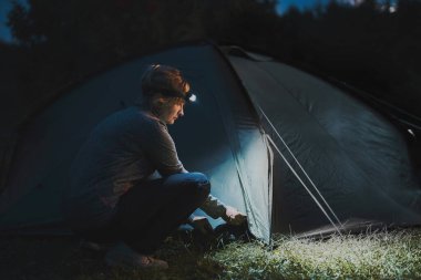 Yaz tatili. Kadın gece kamp çadırında kafa lambası kullanarak çadır açıyor. Yaz gezisi. Kamp alanı hazırlanıyor. Tatili doğaya yakın bir yerde geçirmek.
