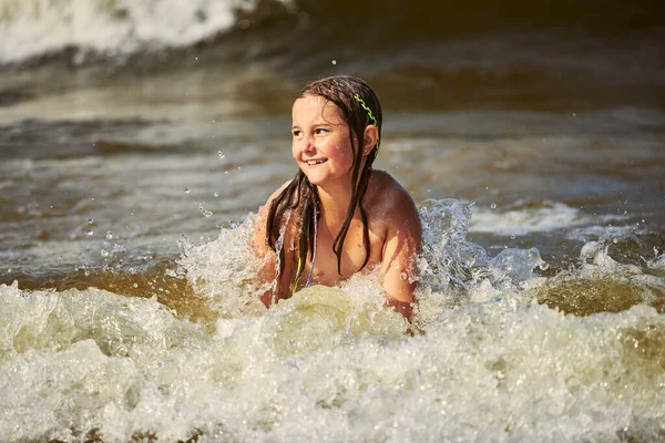 Little girl playing with waves in the sea. Kid playfully splashing with waves. Child jumping in sea waves. Summer vacation on the beach. Water splashes. Travel during summertime concept