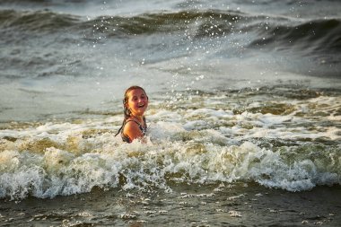 Küçük kız denizde dalgalarla oynuyor. Çocuk neşe içinde dalgalarla sıçrıyor. Çocuk deniz dalgalarında zıplıyor. Yaz tatilinde sahilde. Su sıçrıyor. Yaz konsepti boyunca seyahat
