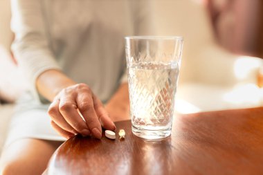 Elinde bir hap ve bir bardak su tutan yetişkin bir kadın. İlaç alan bir kadın. Evde ısmarlıyorum. Hastanedeki hasta iyileşiyor. Akıl sağlığı. Migren, diyabet, ağrı kesici, grip, baş ağrısı, hastalık, hastalık, depresyon ve sağlık konsepti