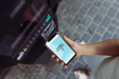 Telefon kullanarak park cezası ödeyen bir kadın. Elektronik ödemeler. NFC teknolojisi. Hızlı mobil ödemeler. Kolaylık ve güvenlik