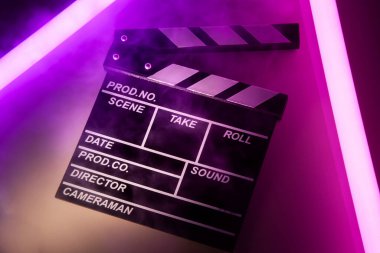 Parlayan neon ışıklandırma arka planında el çırpmalı film tahtası. Video yönetmeni sinema filmi yapıyor. Film alkışları tasarım elementi. Video film yapmak için film yapımcısı alkışlaması