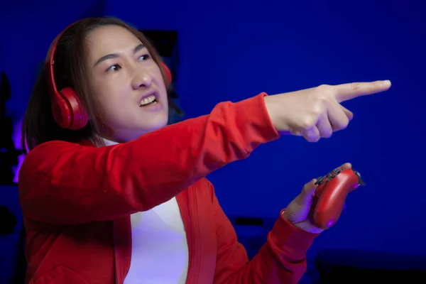 Kulaklıklı heyecanlı Asyalı kadın oyuncu elinde joystick ile online video oyunu oynuyor. Profesyonel flama oyunları sinirlenir ve sosyal oyun oyunlarında zorlanır. Siber Neon Işıkları Biçimi