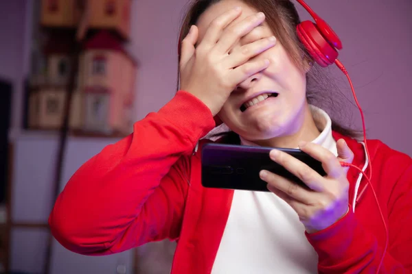 Asian women gamer with headphone playing mobile game on the smartphone online. professional streamers gaming streaming on social playing game having regrets losing the game. Cyber Neon Lights Style
