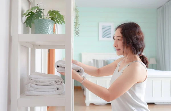 Positive Asian woman housewife tidying modern home. Happy woman doing domestic chores. Asian housewife folding clothes in the closet.