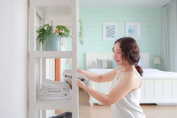 Positive Asian woman housewife tidying modern home. Happy woman doing domestic chores. Asian housewife folding clothes in the closet.