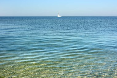 Sakin deniz yüzeyi. Sabahın erken saatlerinde açık gökyüzünün altında yelkenli gemisiyle deniz manzarası.