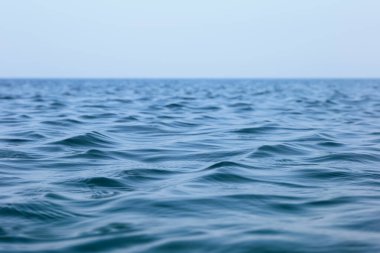 Denizin yüzeyinde küçük dalgalar var. Berrak bir gökyüzü altında sakin bir deniz manzarası.