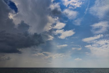 Denizin üstünde yağmurlu bir hava. Deniz manzarası ve güneş ışınları üzerinde gök gürültülü bulutlar.