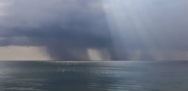 Denizin üstünde yağmurlu bir hava. Ufuktaki güneş ve güneş ışınları muhteşem bir manzara yarattı..