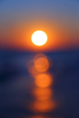 Denizin üzerinde bulanık bir günbatımı. Odaklanamama etkisinden dolayı, su yüzeyindeki parıltı bir bokeh etkisine ve soyut bir arka plana benziyor..