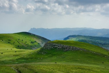 Güneşli bir günde bulutlu resimli bir dağ manzarası. Arka planda Kırım Dağları 'nın en yüksek ve en ünlü zirvelerinden biri olan ünlü dağ' Ai-Petri 'bulunuyor..