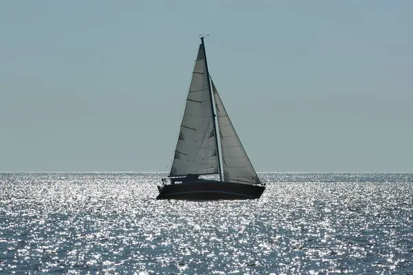 Denizdeki bir yelkenlinin ana hatları ve suyun üzerindeki parlak güneş ışığı. Deniz manzarasında akşam ve yoğun sis..