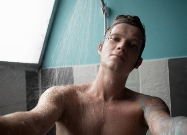 Genç adam saçlarını ve vücudunu yıkıyor, banyoda suyun altında duruyor. Yüksek kalite fotoğraf