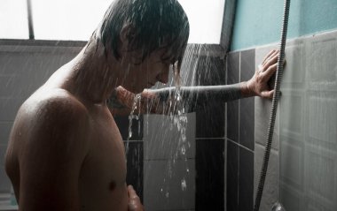 Genç adam saçlarını ve vücudunu yıkıyor, banyoda suyun altında duruyor. Yüksek kalite fotoğraf