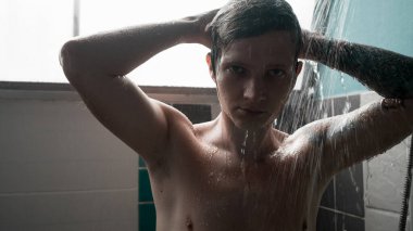 Genç adam saçlarını ve vücudunu yıkıyor, banyoda suyun altında duruyor. Yüksek kalite fotoğraf