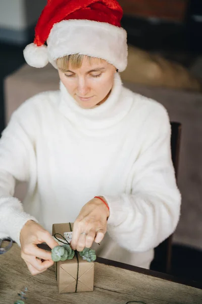 圣诞礼帽女人们在家里用环保材料包装圣诞礼物 图库照片