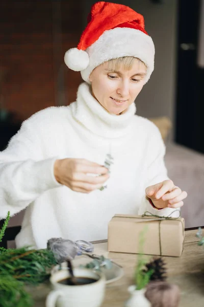 圣诞礼帽女人们在家里用环保材料包装圣诞礼物 免版税图库图片