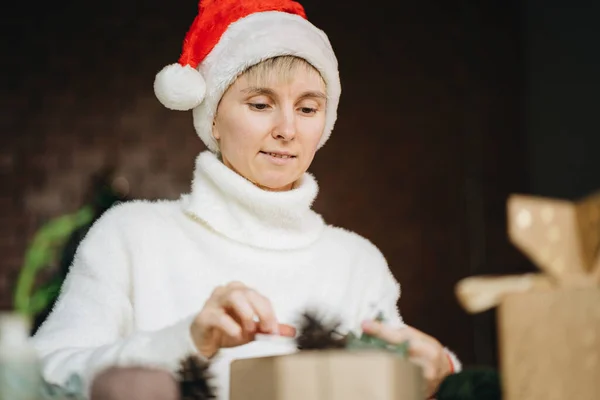 圣诞礼帽女人们在家里用环保材料包装圣诞礼物 免版税图库照片