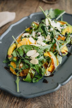 Avokado, roket ve portakallı salata tabağı ahşap masada.