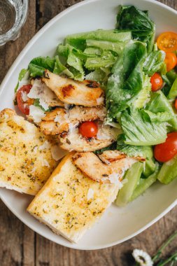 Sezar salatası ahşap masada beyaz bir tabakta servis edilir.