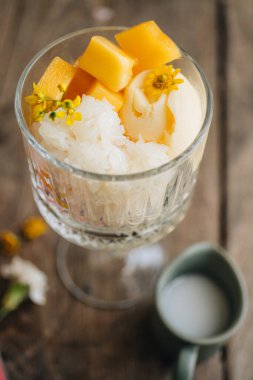 Hindistancevizli dondurma kasesi mangolu pilav ve ahşap masada hindistan cevizi sosu.