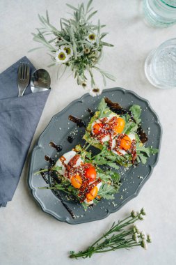 Yüksek açılı mozzarella soslu avokado sandviçi, kuru ve taze domatesler ve beyaz masadaki roka.