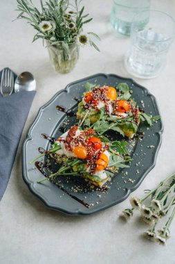 Yüksek açılı mozzarella soslu avokado sandviçi, kuru ve taze domatesler ve beyaz masadaki roka.