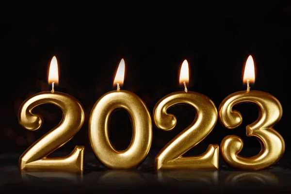 Holiday background Happy New Year 2023. Numbers of year 2023 made by gold burning candles on black background. celebrating New Year holiday, close-up. Space for text