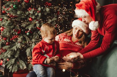 Noel ağacının altında mutlu bir aile. Noel Baba şapkalı bebek Noel ağacının altında hediyeler ve hediyeler. Mutlu tatiller, yeni yıl. Evde sıcak bir kış akşamı. Xmas zamanı.
