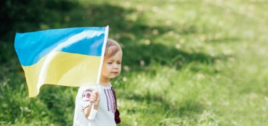 Child carries fluttering blue and yellow flag of Ukraine in field. Ukraines Independence Day. Flag Day. Constitution day. Girl in traditional embroidery with flag of Ukraine