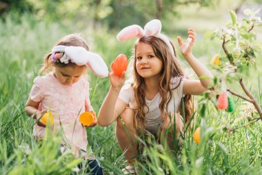 Paskalya yumurtası avı. Bahçede Paskalya yumurtası avında renkli yumurta toplamak için koşan tavşan kulaklı bir grup çocuk. Paskalya geleneği. Sepet bahar konseptiyle parkta gülen çocuklar.