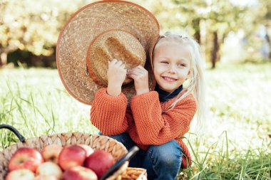 Sonbaharda çiftlikte elma toplayan bir çocuk. Ağaç bahçesinde oynayan küçük kız. Sağlıklı beslenme. Tatlı küçük kız kırmızı lezzetli meyve yiyor. Hasat Konsepti. Elma toplama.