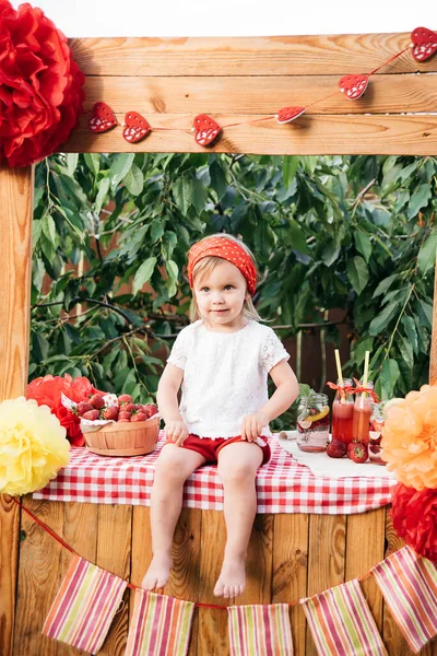 Lemonade Stand. Adorable little girl trying to sell lemonade. strawberry lemonade with ice and mint as summer refreshing drink in jars. Cold soft drinks with fruit. Child drinking smoothie in jar