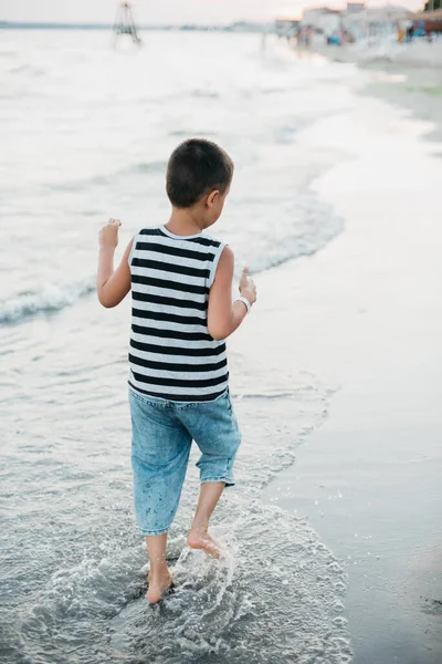 海での夏休み 海辺の縞模様のTシャツの男の子 夏休み中はビーチで遊んでいる子供たち 幸せな子供は日没時に遊ぶ 幸せな子供時代 旅と冒険のコンセプト — ストック写真