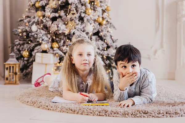 Erkek ve kız Noel ağacının yanında Noel Baba'ya mektup. Mutlu Noeller ve mutlu tatiller. Çocuk yalan katta