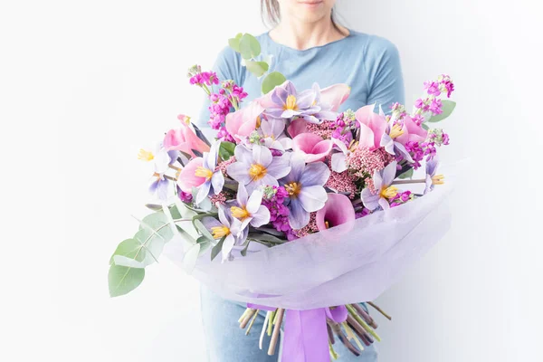 Woman holding large bouquet of flowers wrapped in purple paper. bouquet in shades of pink, purple and white lilies, tulips and other small flowers. floral card. Mothers day, International Womens Day