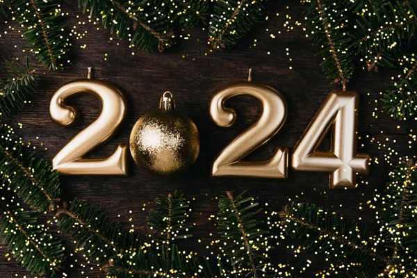 Holiday background Happy New Year 2024. Numbers of year 2024 made by gold candles wooden rustic background with fir tree. celebrating New Year holiday, close-up. Space for text