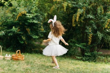 Easter egg hunt. Girl child Running To Pick Up Egg In Garden. Easter tradition. Baby with basket full of colorful eggs.