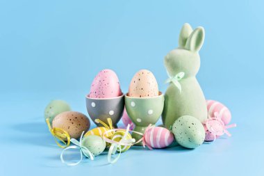 Mutlu Paskalya tebrik kartları. yumuşak pastel Paskalya tavşanı heykelciği ve renkli paskalya yumurtalarının canlı mavi arka planda toplanması.