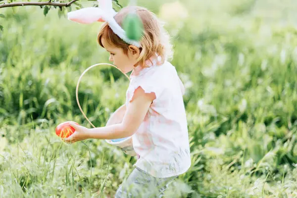 复活节彩蛋狩猎 女孩穿着兔子耳朵跑去花园捡鸡蛋 复活节传统 满满一篮子彩蛋的婴儿 广角视野 图库图片