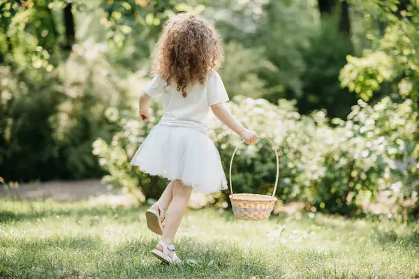 复活节彩蛋狩猎 女孩穿着兔子耳朵跑去花园捡鸡蛋 复活节传统 满满一篮子彩蛋的婴儿 免版税图库照片