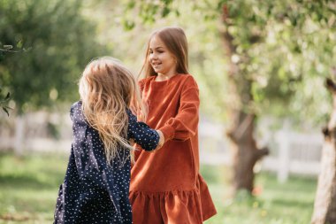 Çocuklar döner, çayırda dans eder. Kızlar eğleniyor. Gün batımı parkında dans eden sevimli, uzun saçlı sarışın kız. Seçici odaklanma. çocukluğun masumiyeti ve mutluluğu