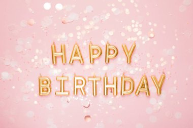 Altın Mutlu Yıllar mektup mumları dağınık konfetiyle pembe bir arka planda düzenlenmiş neşeli ve şen şakrak bir kutlama sahnesi yaratıyor. Doğum gününü zarafet ve cazibeyle kutluyoruz.